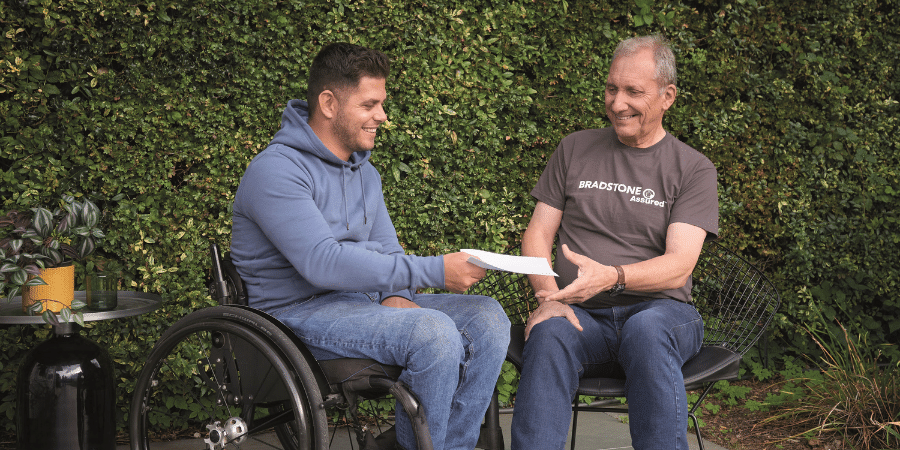 man in wheelchair handing paper to bradstone assured landscaper